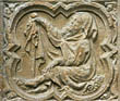Panel 12:03 - Elderly man with hood and staff, seated on the ground